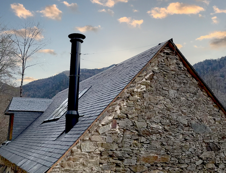 rénovation toiture en ardoise sur grange en pierre de montagne avec conduit de poêle noir au coucher de soleil
