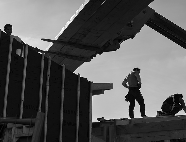 équipe de charpentiers levant un panneau de charpente bois à l'élévateur sur chantier de construction neuve