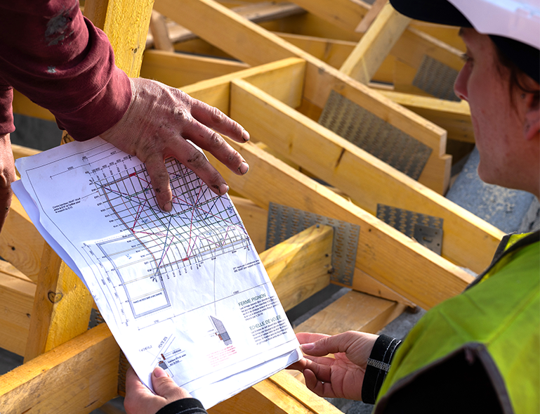 charpentier et conducteur de travaux vérifiant les plans de fermes de charpente bois sur chantier