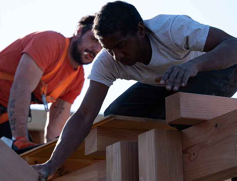 deux charpentiers assemblant à la main des pièces de charpente bois massif sur chantier