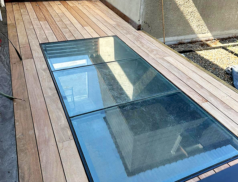 trappe de toit vitrée encastrée dans une terrasse en bois permettant le passage de lumière naturelle