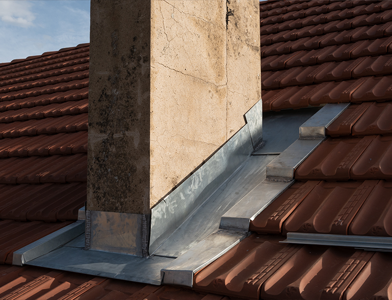 solin zinc façonné autour d'une cheminée en pierre sur toiture en tuile rouge brun