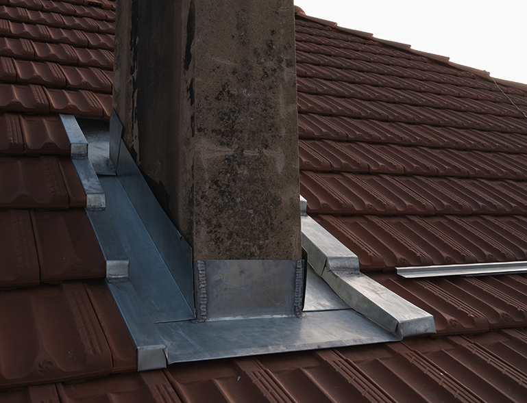 solin zinc façonné autour d'une cheminée en pierre sur toiture en tuile rouge brun